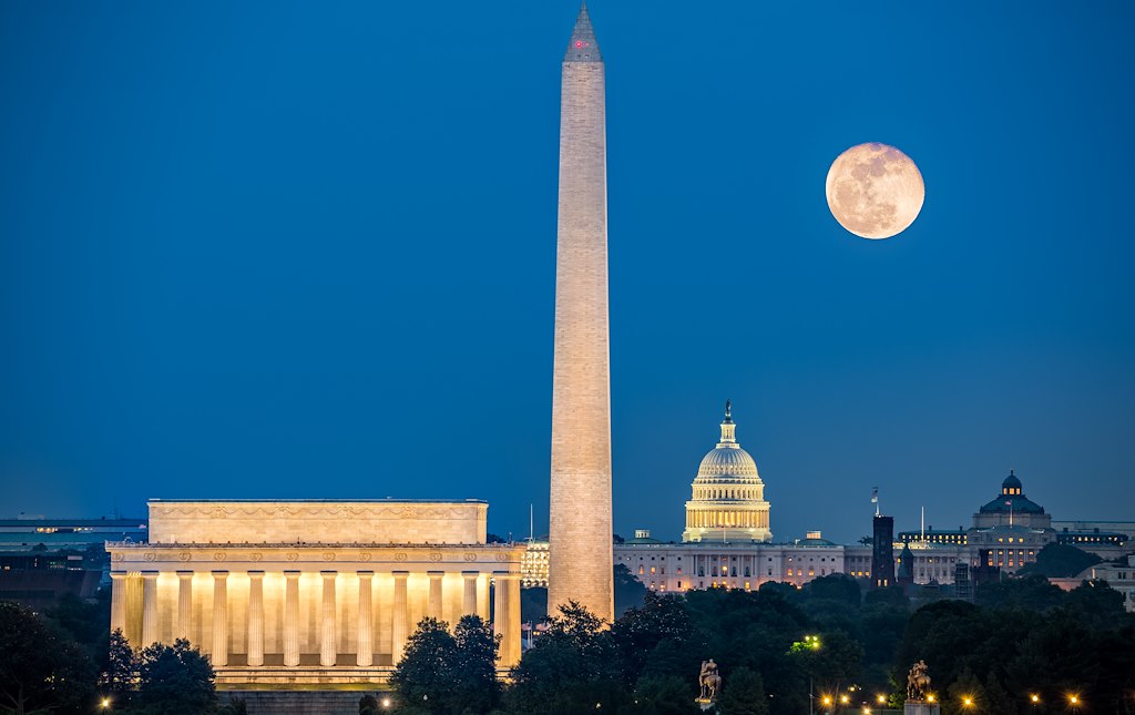 A nighttime view of the Washington Monument, Lincoln Memorial, and Capitol Building with the moon in the sky