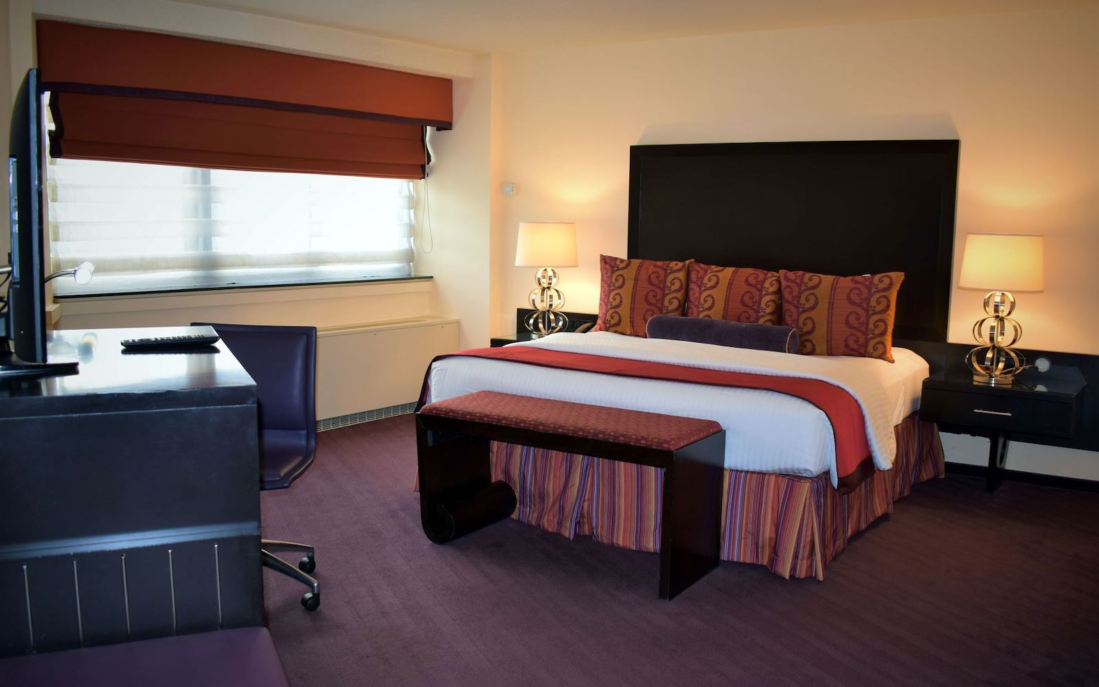 A hotel room with a bed, desk, and window