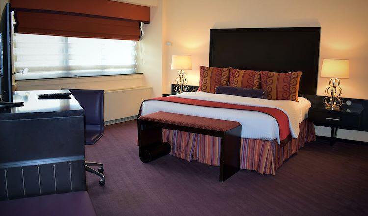 A hotel room with a bed, desk, window, and TV